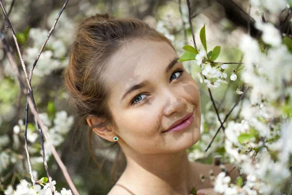 Schönes junges Mädchen, das neben blühenden Bäumen in der Frühlingsgarde steht — Stockfoto