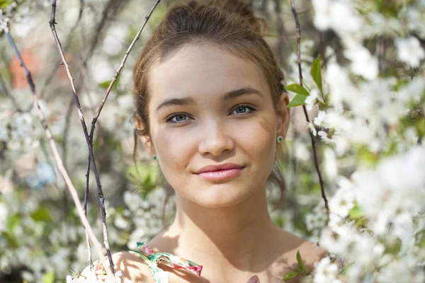 Vacker flicka står nära blommande träd i vårträdgård — Stockfoto