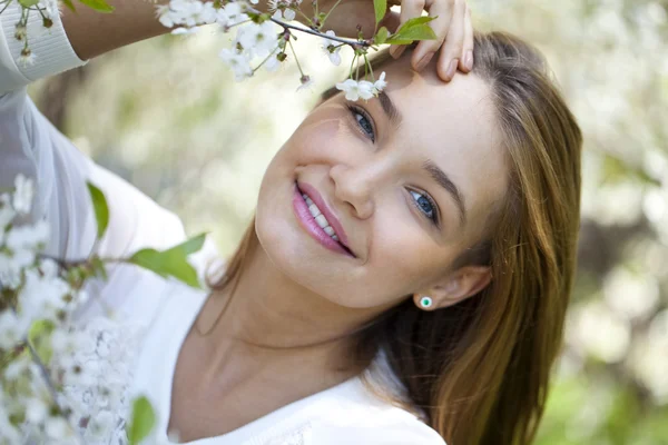 Schönes Mädchen, das neben blühenden Bäumen im Frühlingsgarten steht — Stockfoto