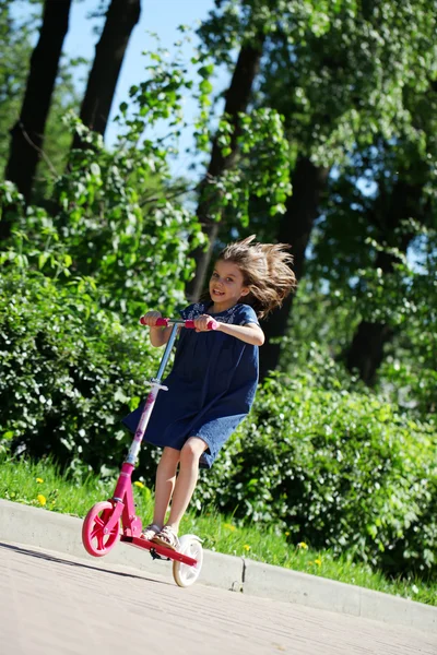 Ragazza felice cavalcando uno scooter in un parco — Foto Stock