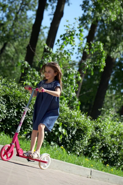 Ragazza felice cavalcando uno scooter in un parco — Foto Stock