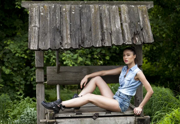 Beautiful young woman sits on a wooden pit in the park — Stock Photo, Image