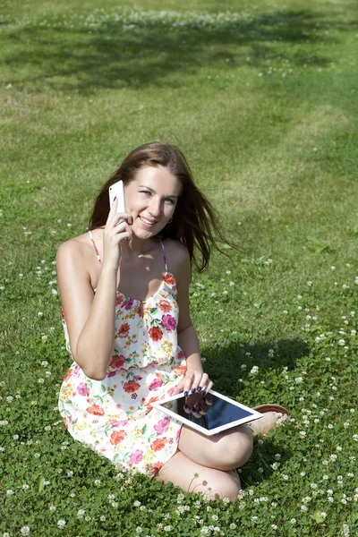 Mulher sentada na grama com o telefone na mão — Fotografia de Stock