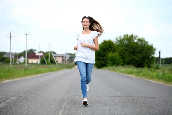 Jovem mulher correndo ao longo de uma estrada rural — Fotografia de Stock