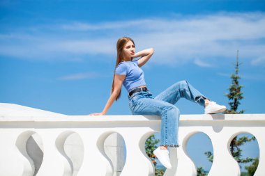 Kot pantolonlu güzel bir kızın portresi bir yaz parkında oturuyor.