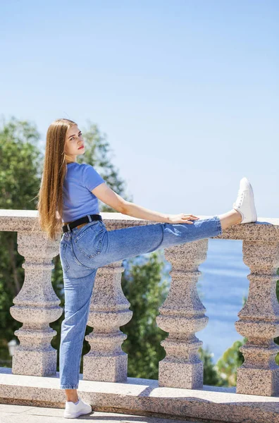 Açık havada, yaz parkında, kot pantolonlu güzel bir sarışının vücut portresi.