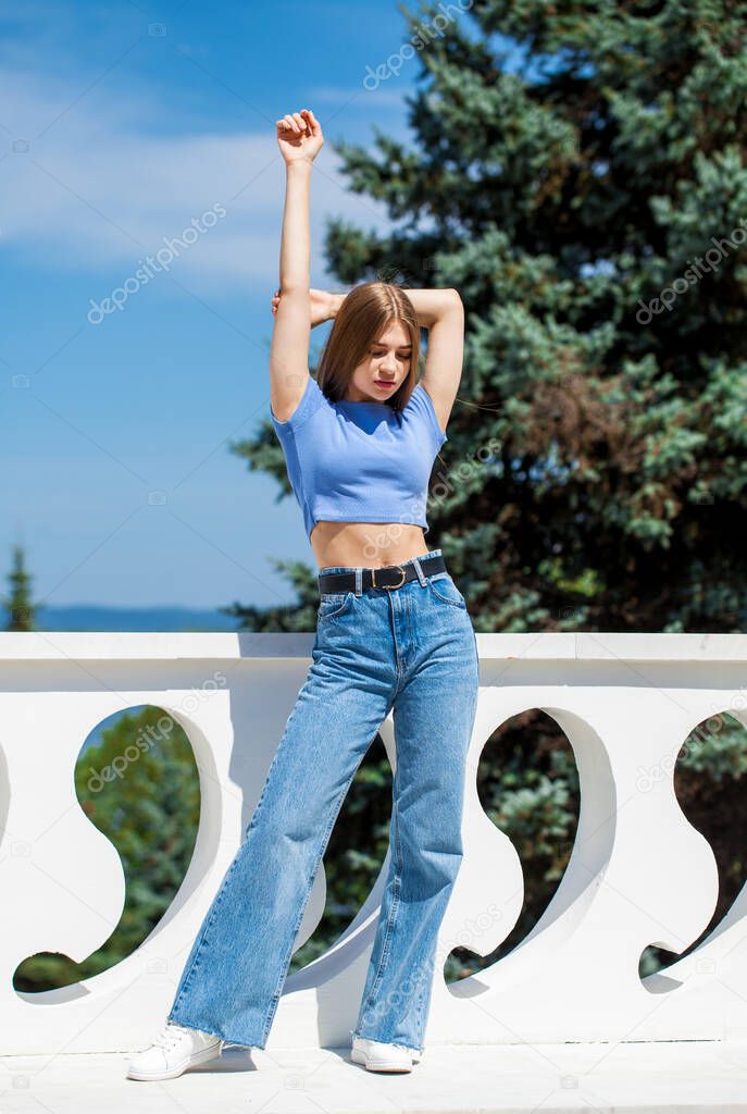 Full length portrait, young beautiful girl in blue jeans posing in a summer park