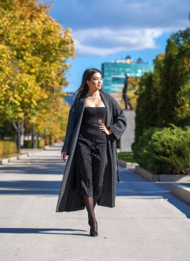 Gri montlu güzel bir kızın uzun boylu portresi setin üzerinde yürüyor.