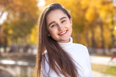 Sonbahar parkında poz veren esmer kızın yakın portresi.