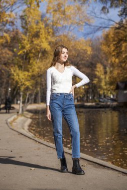 Beyaz kazaklı, mavi kotlu, sonbahar parkındaki güzel sarışın kız. 