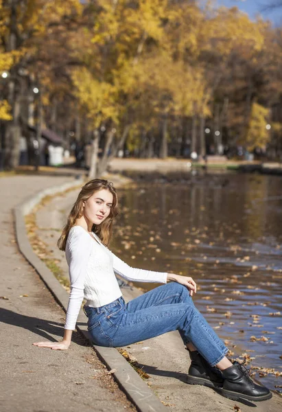 穿着白色毛衣和蓝色牛仔裤的年轻漂亮的金发姑娘 秋天公园的室外 — 图库照片