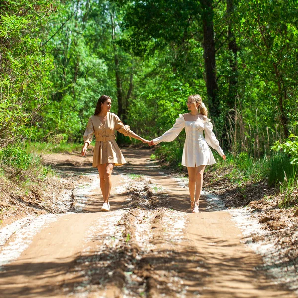 夏のドレスを着た2人の若い美しい女の子が田舎道を歩いている — ストック写真
