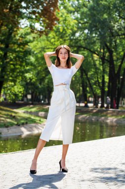 Tam boy portre, beyaz etekli güzel bir kız yaz parkında poz veriyor.