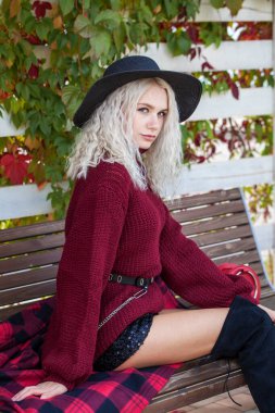 Sonbahar parkında bir bankta oturan bordo kazaklı şık bir kız.