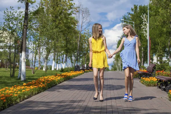 夏のドレスの二人の陽気なガールフレンドは天気の良い日に通りを歩いています — ストック写真