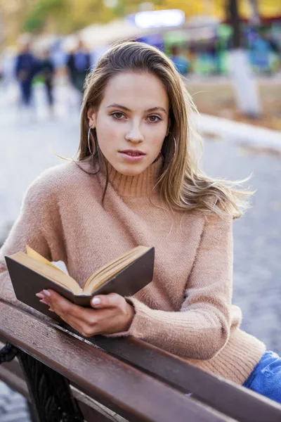 一个漂亮的小女孩带着一本书坐在秋天公园的长椅上 — 图库照片