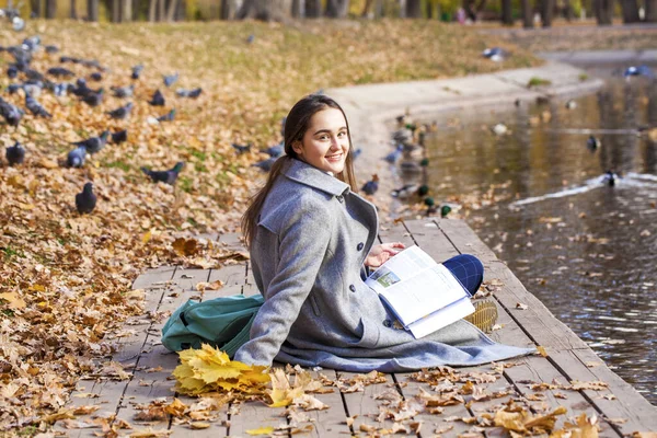 教科書付きの秋の公園に座っている若い美しい女の子 — ストック写真