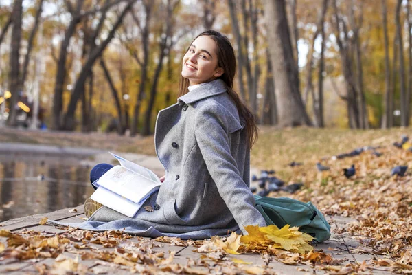 教科書付きの秋の公園に座っている若い美しい女の子 — ストック写真