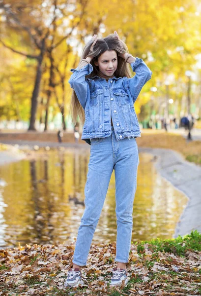 Güz parkında poz veren şık, yırtık pantolonlu güzel bir kızın tam boy portresi.