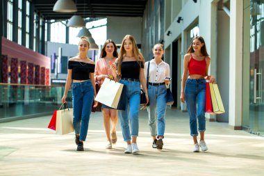 Mutlu genç kız arkadaşlar alışveriş merkezinde yürüyor.