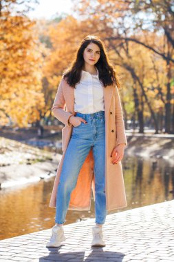 Bir sonbahar parkının arka planında poz veren güzel bir kızın tam boy portresi.