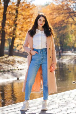 Bir sonbahar parkının arka planında poz veren güzel bir kızın tam boy portresi.