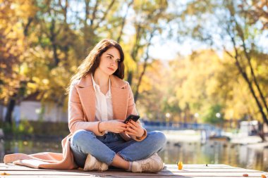Sonbahar parkında poz veren kot pantolonlu genç bir kızın tam boy portresi.