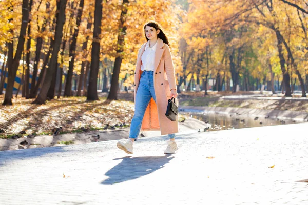 Bir sonbahar parkının arka planında poz veren güzel bir kızın tam boy portresi.