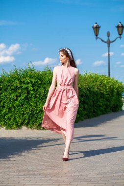 Pembe elbiseli güzel esmer bir kadının tam boy portresi.