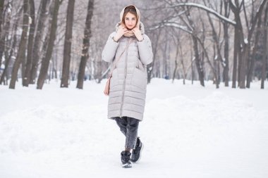 Kış parkında poz veren güzel bir kızın tam boy portresi.