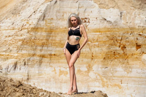 一个身穿黑色比基尼的年轻漂亮金发姑娘在沙坑背景上的画像 — 图库照片