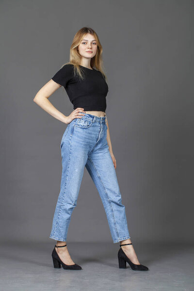 Full body portrait of a young beautiful blonde model in blue jeans, isolated on gray background
