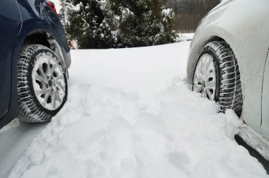 Close-up of two cars wheels stuck in snow against winter trees