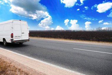 Countryside asphalt road with a white delivery van against a blue sky with clouds