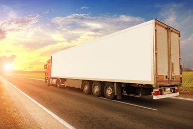 Big red truck with a white trailer with space for text on a countryside road against a blue sky with a sunset