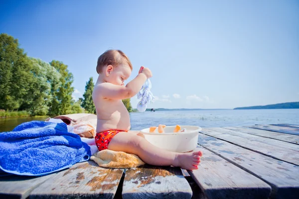 Little girl playing with toys on the wooden pier at the river — Stock Photo, Image