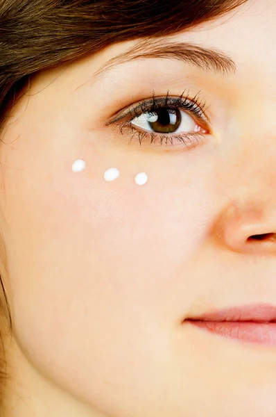 De helft van een vrouw gezicht met crème onder het oog — Stockfoto