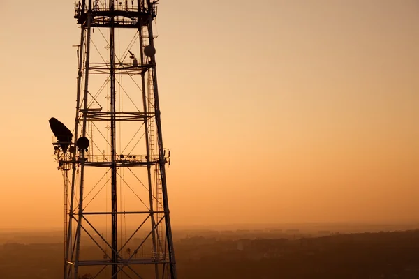 Communication tower at sunset with cityscape — Stock Photo, Image