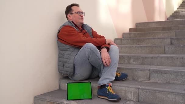Depresyonda merdivenlerde oturan beyaz erkek işçi kovulmuş. Tablet bilgisayarında yeşil ekran var.. — Stok video