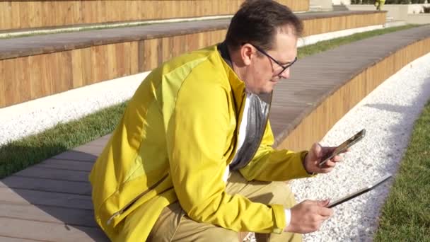 Man met smartphone en tablet in modern stadspark — Stockvideo