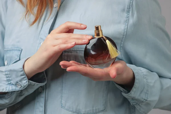 Perfume bottle in hands of woman wearing blue jeans wear