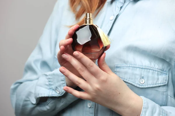 Perfume bottle in hands of woman wearing blue jeans wear