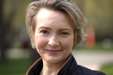 Modern gündelik giyimde güzel orta yaşlı kadın portresi, yaz parkının yeşili karşısında..