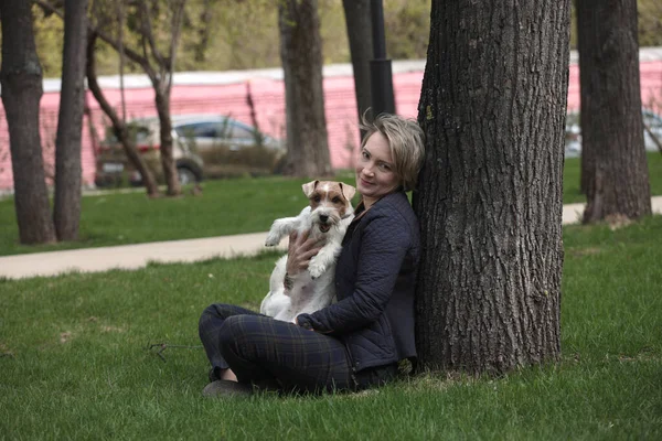 Atrakcyjna Kobieta Siedząca Pod Drzewem Przytulająca Białego Psa Terrorysty Jack — Zdjęcie stockowe