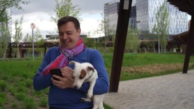 Kollarında küçük beyaz bir köpekle telefonda konuşan bir adam.