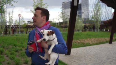 Kahve fincanını çıkaran adam kucağında küçük beyaz bir köpek tutuyor.