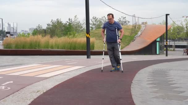 プラスサイズの男は川沿いの公園で松葉杖を歩く — ストック動画
