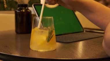 Erkekler, yeşil ekranlı tablet bilgisayarın arka planında samanla içecekleri karıştırıyorlar. Ofis dışında çalış, serbest çalış. Yemek vakti, narenciye suyu..