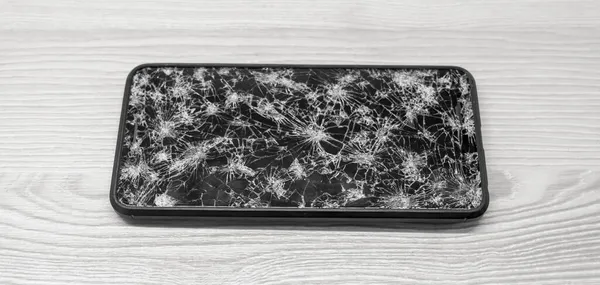 Smartphone de tela de toque moderno com tela quebrada cheia de rachaduras no fundo de madeira. Reparação conceito gadget — Fotografia de Stock