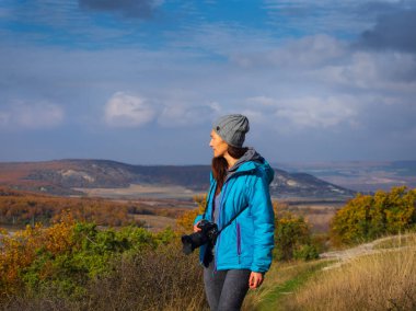 Kameralı kız dağlara bakıyor. Güneşli bir sonbahar gününde dağın güzel manzarası. Kırım 'ın Bakhysarai bölgesindeki Eski-Kermen mağarası.